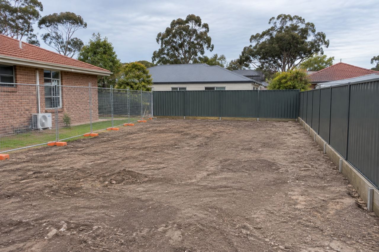 A vacant cleared rear lot behind a brick house with new Colorbond fencing